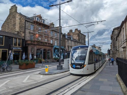 a white tram on a city street with buildings at 89 The Merchants by The House of Danu in Edinburgh