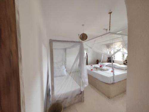 een witte slaapkamer met 2 bedden en klamboes bij RiccArDella House Rafiki Tamu in Watamu