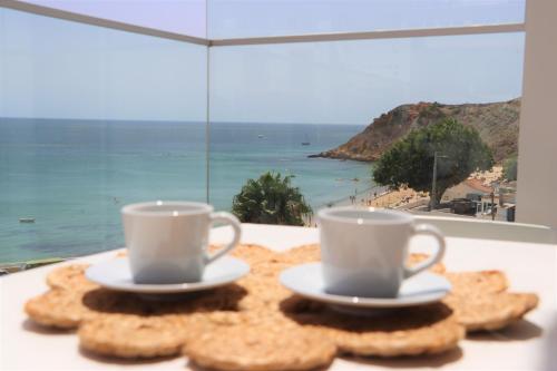 two coffee cups and cookies on a table with a window at MC Suites Burgau with amazing front sea view in Burgau