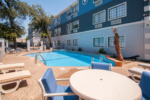 a pool with chairs and a table and a building at Days Inn & Suites by Wyndham San Antonio North/Stone Oak in San Antonio