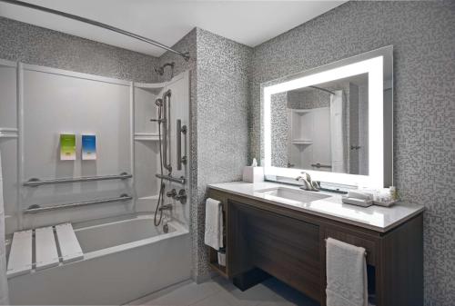 a bathroom with a sink and a tub and a mirror at Home2 Suites By Hilton Utica, Ny in Utica