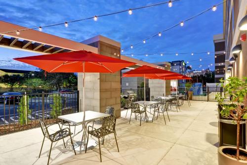 un patio con mesas y sillas y sombrillas rojas en Home2 Suites By Hilton Tampa USF Near Busch Gardens en Tampa