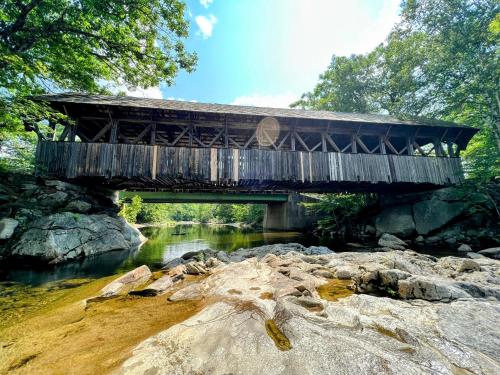 a wooden bridge over a river with rocks at Ski Chalet 6 min to Sunday River - Hot Tub, Home Theater, Game Room, Fire Pit - Sleeps 12 in Bethel