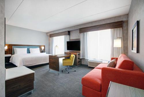 Hampton Inn & Suites By Hilton Waterloo St. Jacobs في واترلو: غرفه فندقيه بسرير واريكه وتلفزيون