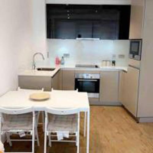 a kitchen with a white table and chairs and a refrigerator at Tee SweetLux Apartment In Canning Town in London