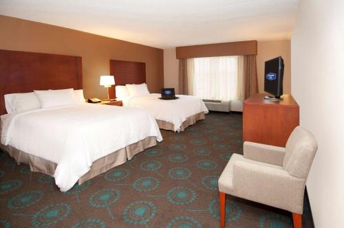 a hotel room with two beds and a chair at Hampton Inn by Hilton Brampton - Toronto in Brampton