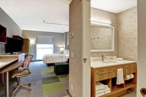 a hotel room with a bathroom with a sink and a bed at Home2 Suites By Hilton Montreal Dorval in Dorval