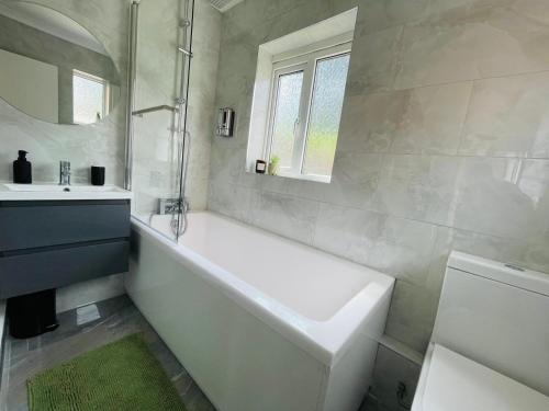 a white bathroom with a tub and a sink at Lovely 4 Bed, Family & Contractors Luton Airport & M1 by Properties2you in Luton