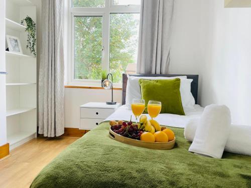 a tray of fruit on a bed with two glasses of orange juice at Lovely 4 Bed, Family & Contractors Luton Airport & M1 by Properties2you in Luton