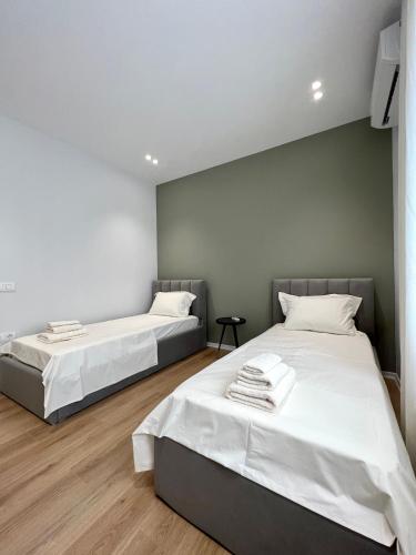 two beds in a room with white walls and wooden floors at George apartments2023 in Korçë