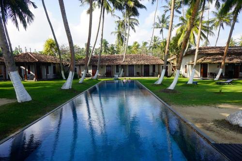 a swimming pool in front of a resort with palm trees at Apa Villa Thalpe in Unawatuna