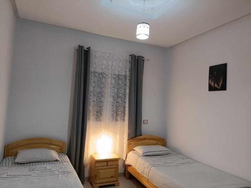 a bedroom with two beds and a window and a lamp at VILLA TILEL AYADI Ridha in El Ahmar