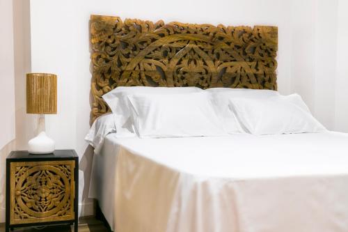 1 cama con sábanas blancas y cabecero de madera en BOUTIQUE REYES CATÓLICOS, en Granada