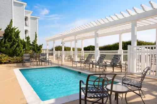 Hampton Inn & Suites Outer Banks/Corolla في كورولا: فناء فيه كراسي ومسبح فيه بيرغولا