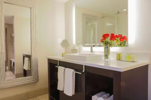 a bathroom with a sink and a vase of red flowers at DoubleTree by Hilton Rochester in Henrietta
