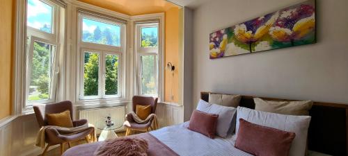 a bedroom with a bed and two chairs and windows at Livada Studio Apartments in Braşov