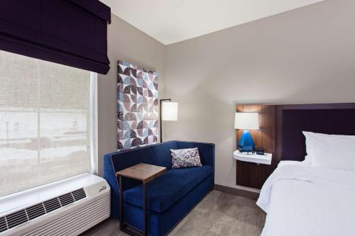 a bedroom with a blue chair and a bed and a window at Hampton Inn & Suites Leavenworth in Leavenworth