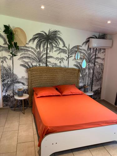 a bedroom with an orange bed with palm trees on the wall at Gites le petit voyageur in Sainte-Anne