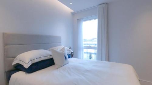 Dormitorio blanco con cama y ventana en Chelsea Harbour 2-Bed Apartment in London, en Londres