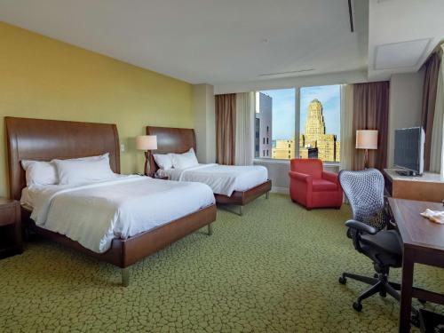 a hotel room with two beds and a desk and a window at The Hilton Garden Inn Buffalo-Downtown in Buffalo