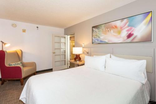 a hotel room with a white bed and a chair at Hilton Garden Inn Daytona Beach Airport in Daytona Beach