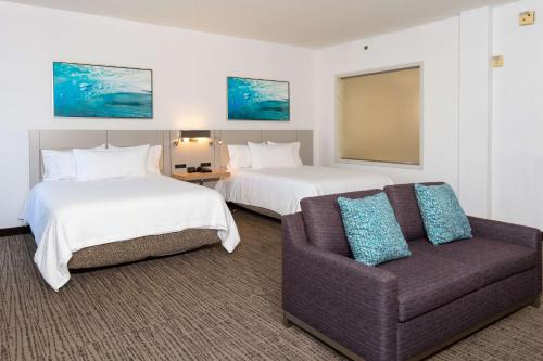 a hotel room with two beds and a couch at Hilton Garden Inn Daytona Beach Airport in Daytona Beach