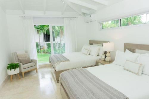 a white bedroom with two beds and a chair at Sunny Vacation Villa No 92 in San Rafael del Yuma