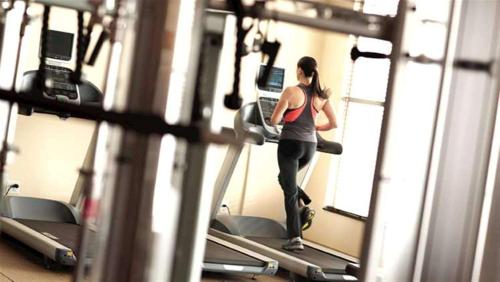 東拉瑟福德的住宿－新澤西州梅多蘭茲東拉瑟福德希爾頓惠庭套房酒店，一名在健身房跑步机上跑步的女人