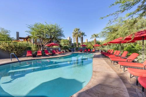 a swimming pool with red chairs and umbrellas at Hilton Grand Vacations Club Palm Desert in Palm Desert