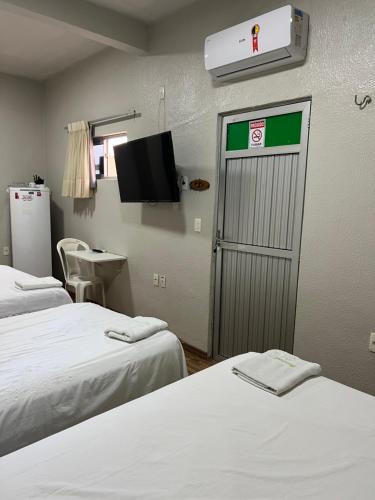 a room with two beds and a door with a tv at Pousada da Celma in Fortaleza