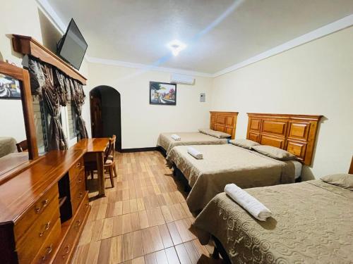 a room with two beds and a desk and a television at Hotel del Carmen in Retalhuleu