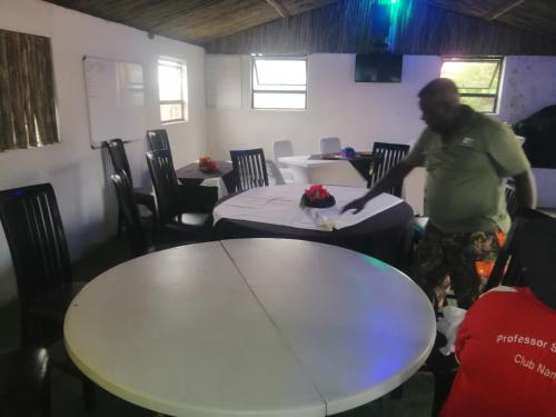 un hombre de pie en una habitación con dos mesas en Okahatjipara Lodge, 