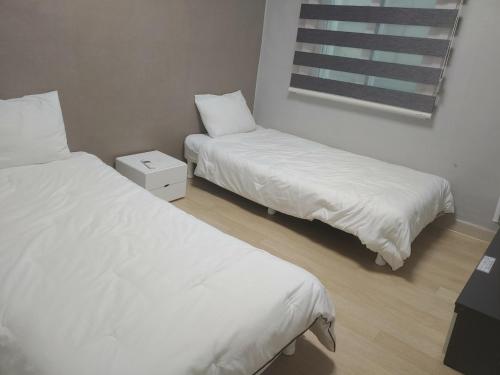 two beds in a room with white sheets and a window at T stay guesthouse in Cheongju
