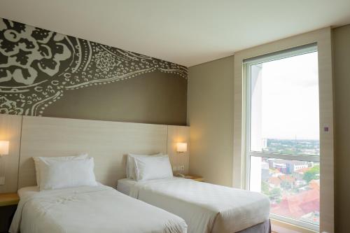 two beds in a hotel room with a window at Swiss-Belinn Saripetojo Solo in Solo