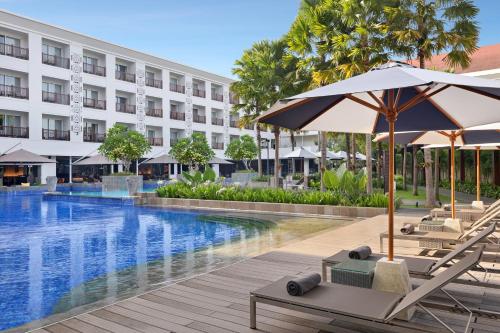 a hotel pool with lounge chairs and umbrellas at Grand Mercure Bali Seminyak in Seminyak