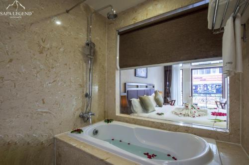 Sapa Legend Hotel & Spa في سابا: حوض استحمام في الحمام مع مرآة كبيرة