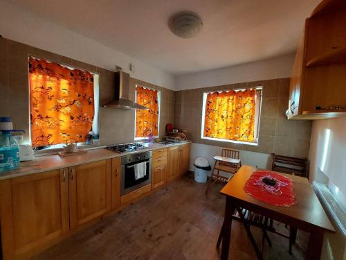 una cocina con armarios de madera, 2 ventanas y una mesa en Casa Vlazilor en Breaza