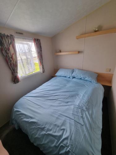 a small bedroom with a blue bed with a window at Pg151 PALM GROVE THE GOLDEN PALM CHAPEL ST LEONARDS in Chapel Saint Leonards