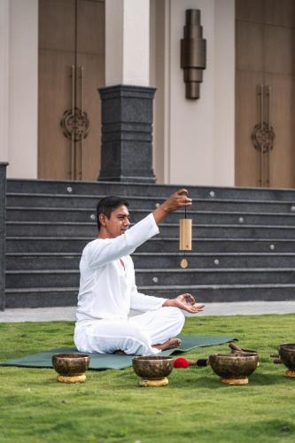 a man sitting on the grass holding a wooden object at Dusit Thani Himalayan Resort Dhulikhel, Nepal in Dhulikhel