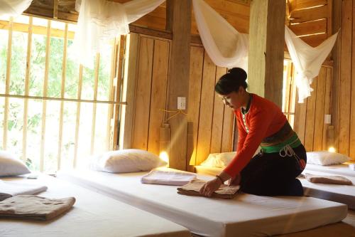 une femme fait un lit dans une pièce dans l'établissement Homestay in Da Bia - Community Based Tourism, à Hòa Bình