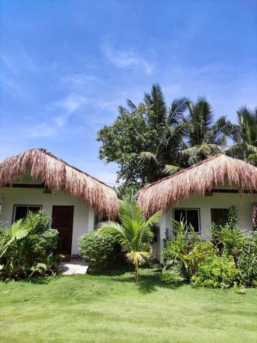 a house with two thatched roofs and palm trees at Prana Siargao Resort in General Luna