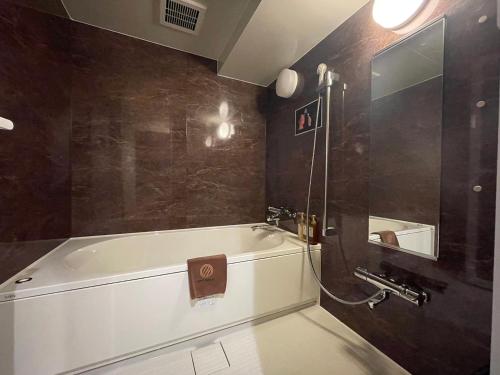 een badkamer met een wit bad en een spiegel bij Nipponbashi Luxe Hotel in Osaka