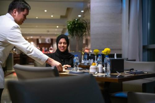 a man serving a woman at a table in a restaurant at Makkah Clock Royal Tower, A Fairmont Hotel in Makkah