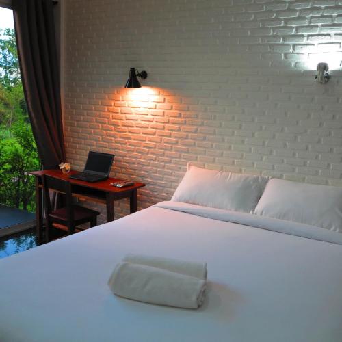 a bedroom with a white bed and a laptop on a desk at Coco Coozy in Kanchanaburi