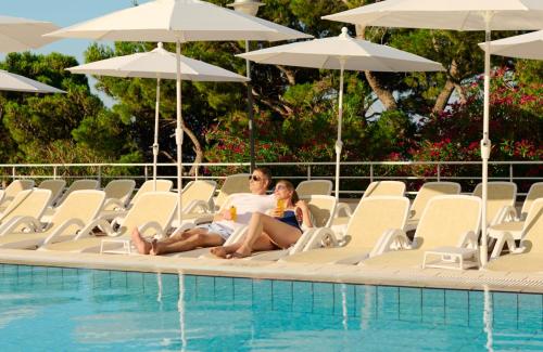 a man and woman sitting on chairs next to a swimming pool at Bluesun Holiday Village Afrodita in Tučepi