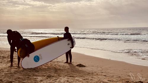 dos personas de pie en la playa con una tabla de surf en Roxon Sea Sand Bat Yam, en Bat Yam