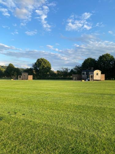 a large field of grass with buildings in the background at The Black Swan Shepherd Hut in Ketton