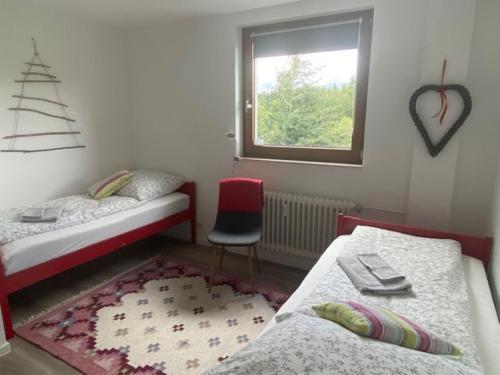 a bedroom with two beds and a window and a red chair at Ferienwohnung Schwarzwald Oase Kniebis in Kniebis