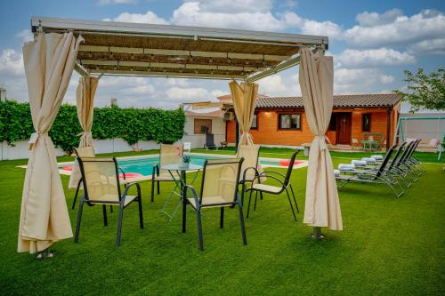 a table and chairs under a pavilion with a pool at Madera y Miel Casa Rural con niños en Puy du Fou in Guadamur