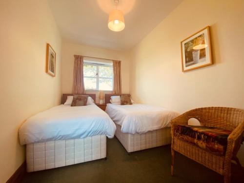 a bedroom with two beds and a chair and a window at Forge Cottage in Rothbury